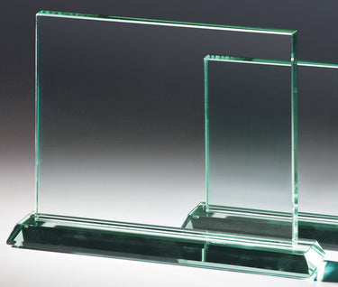 Zwei klare Glaspreise Braunschweig 3-er Serie 120x150 mm - 220x250 mm PK766423-21-3 mit rechteckigen Tafeln und dicken Sockeln auf einem grauen Hintergrund mit Farbverlauf, hergestellt aus Jade Premium Glas. Jeder Preis wird wunderschön in einer blauen Geschenkbox präsentiert.
